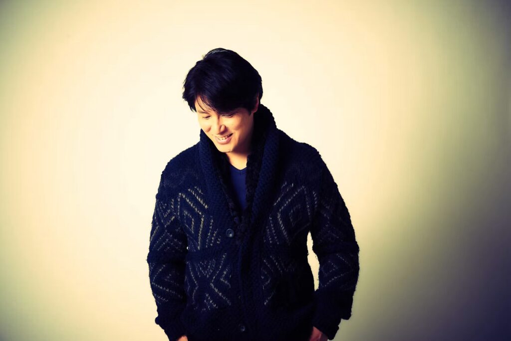 Eisuke Mochizuki smiling in a knit cardigan
